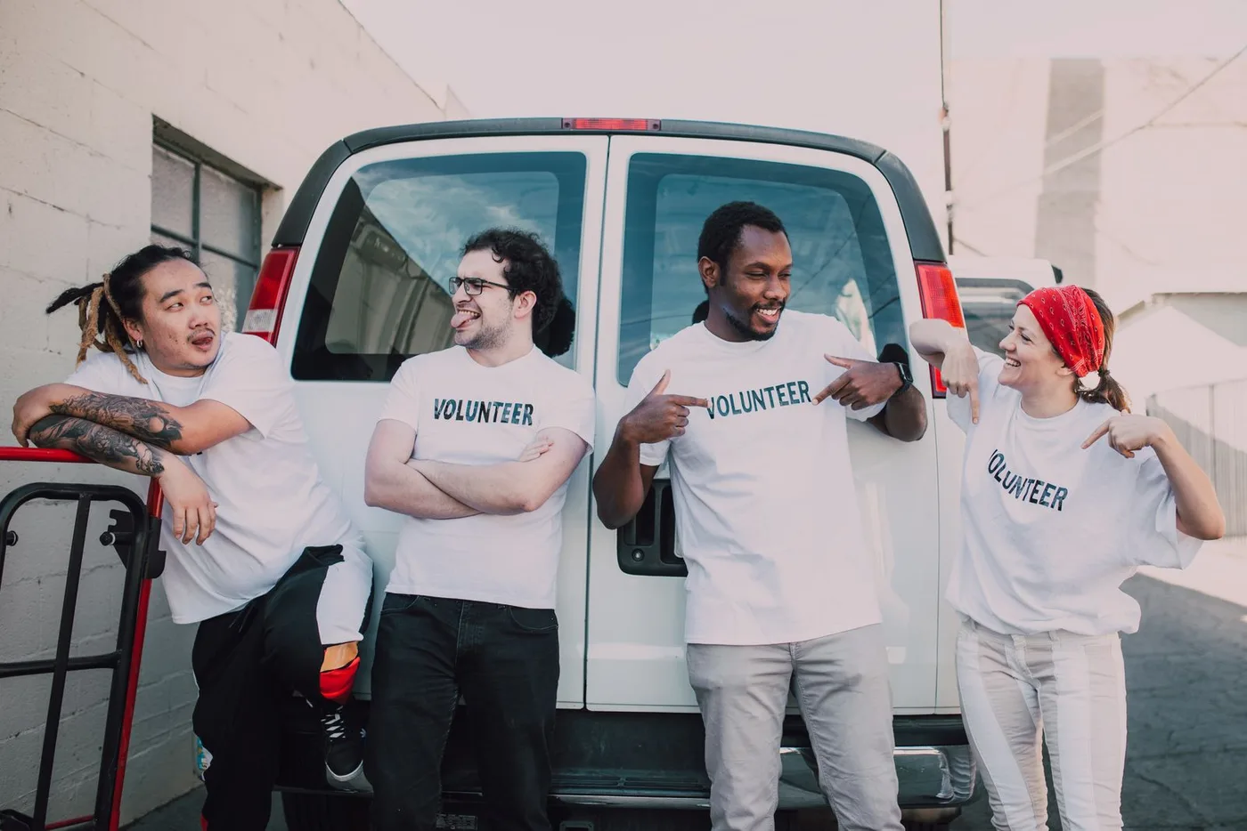 Four community-service volunteers wearing coordinated Volunteer shirts beside a van